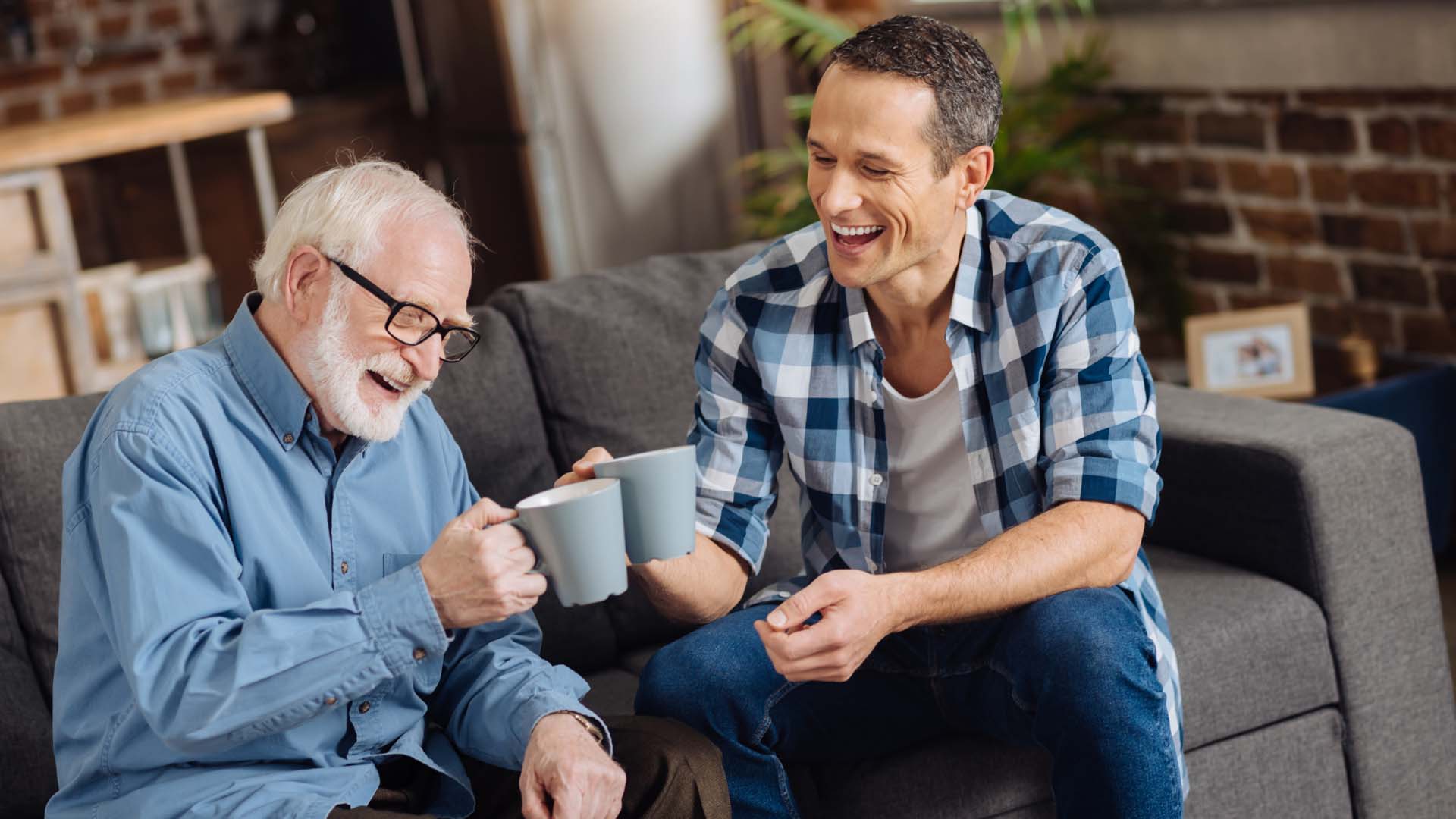 Two men of differing ages have a cup of tea and laugh 