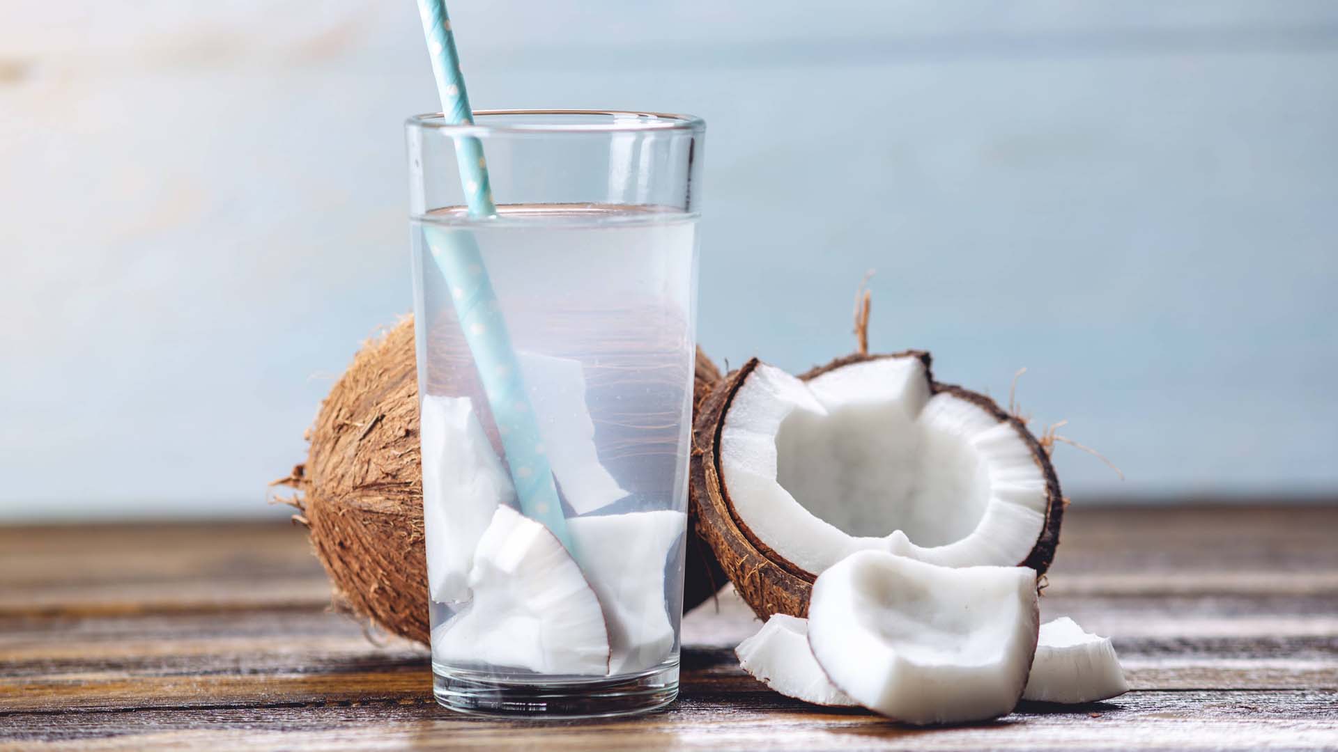 a glass containing coconut water next to a fresh coconut which has been split in two