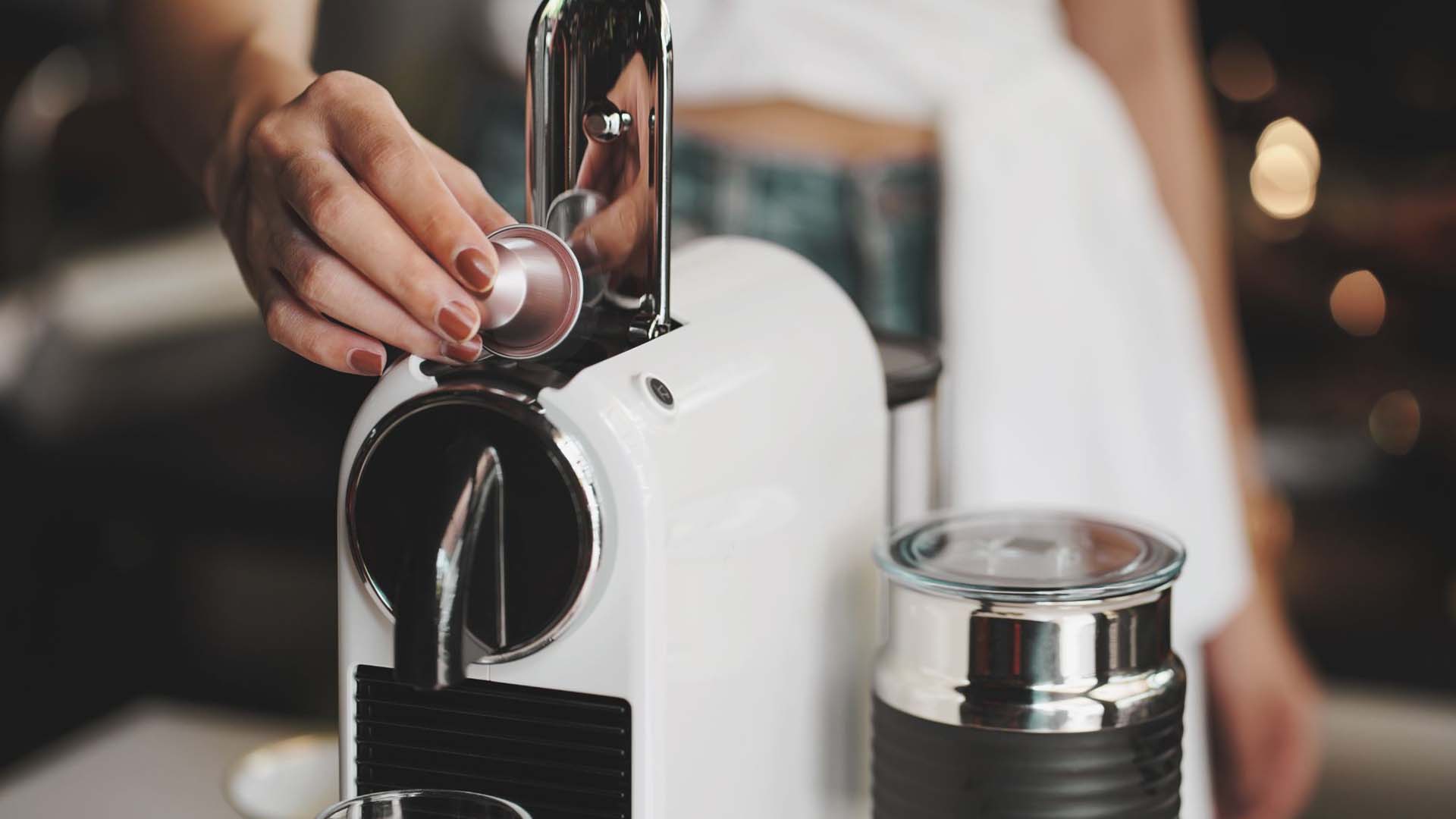 Close-up of a pod being inserted into a white and chrome espresso machine.