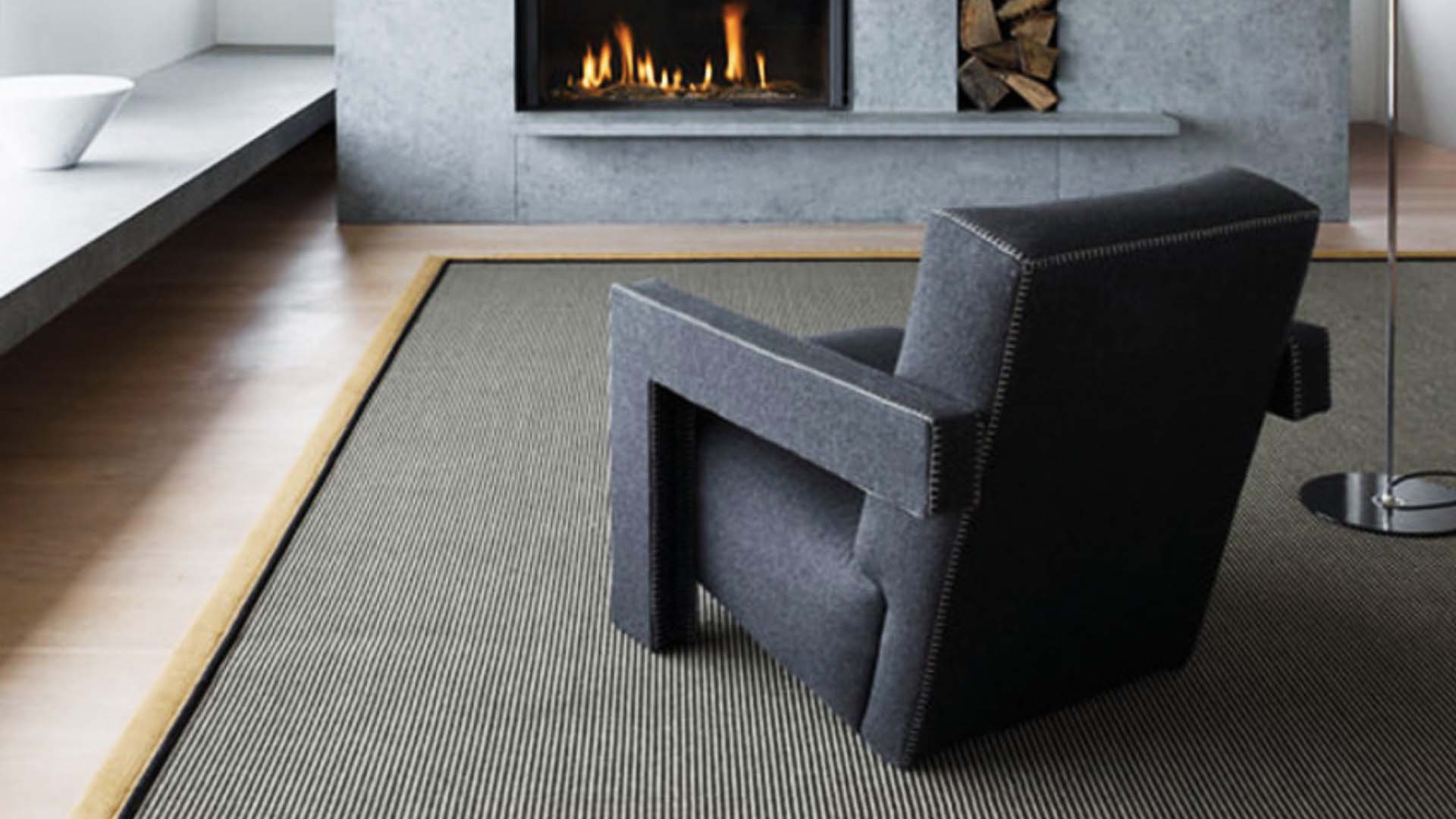 A huge grey rug with black edging beneath a black chair