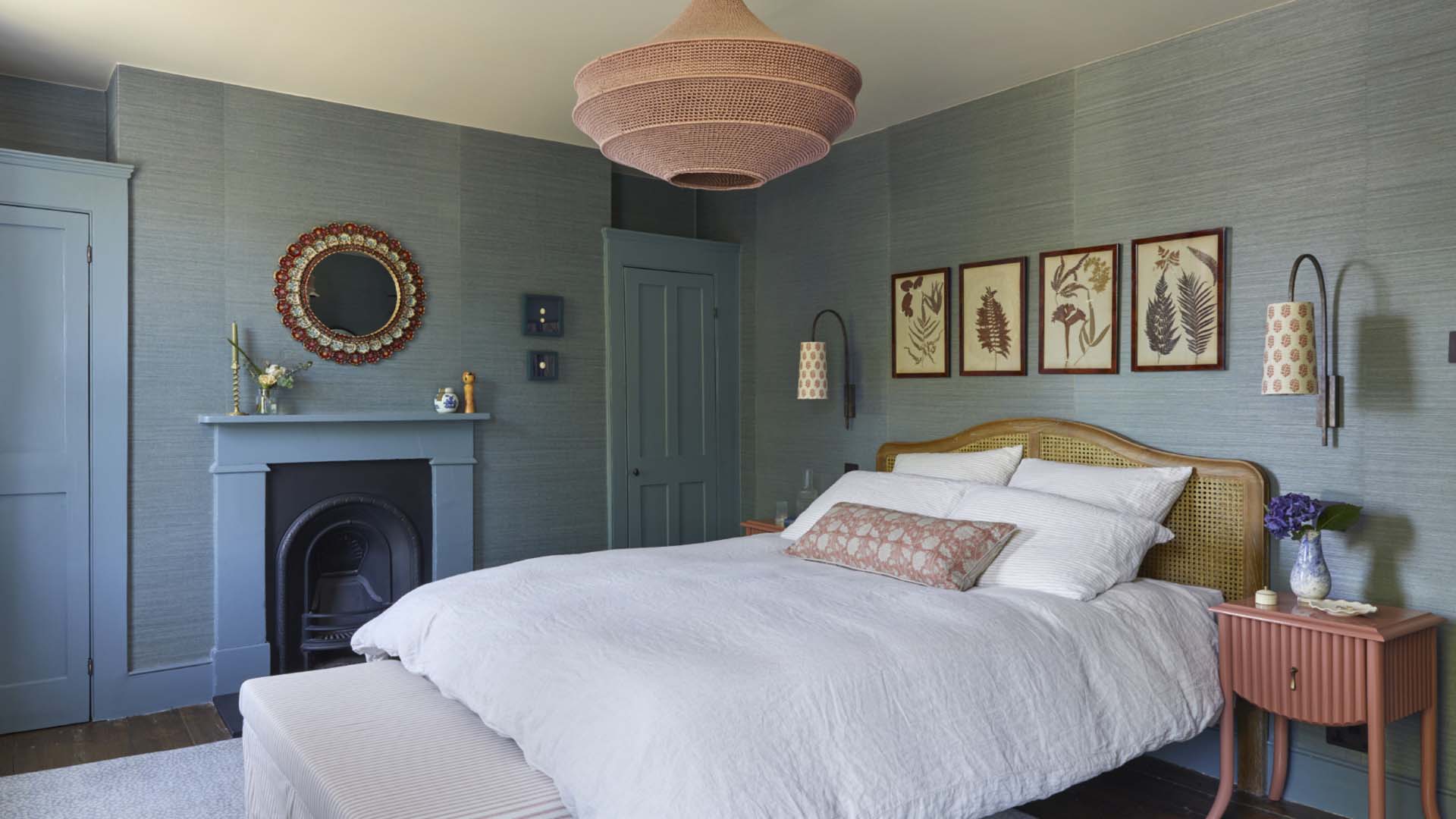 A bedroom painted in calming blue shades with a black fireplace, built-in wardrobe and artwork framed above a double bed