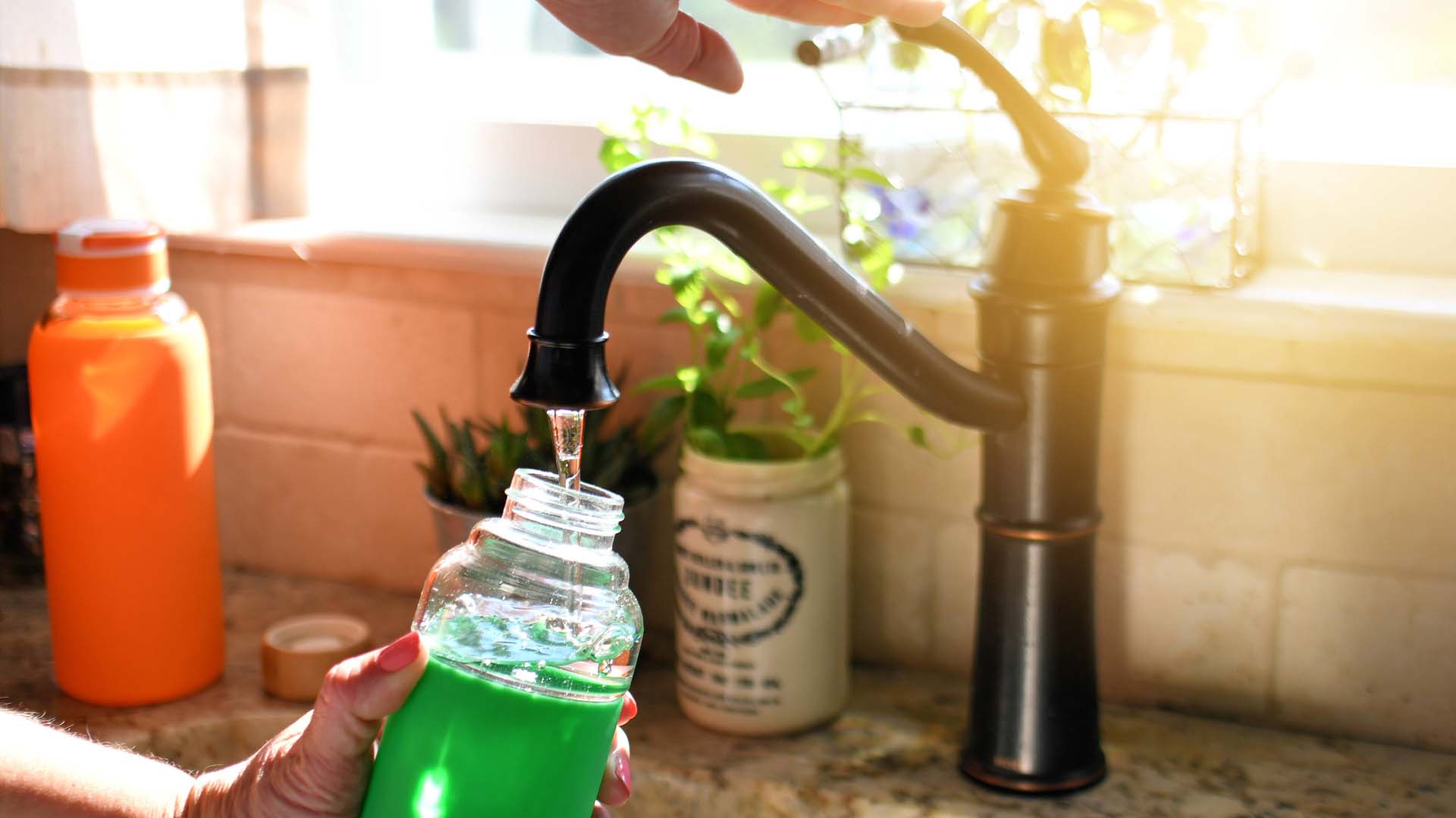 someone filling up a water bottle from a tap in a kitchen