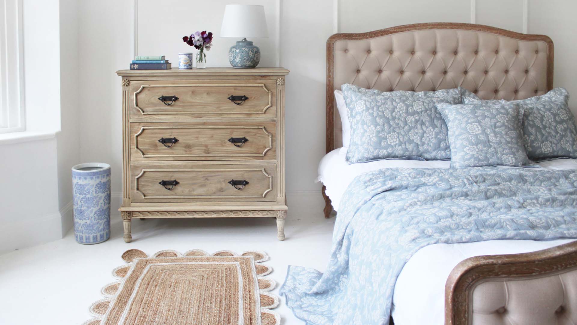 French-style bedroom furniture with a rattan double bed and distressed wood chest of drawers.
