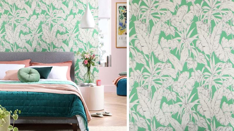 A bedroom with green and white palm leaf wallpaper and a double bed with bedding in shades of pink and green.