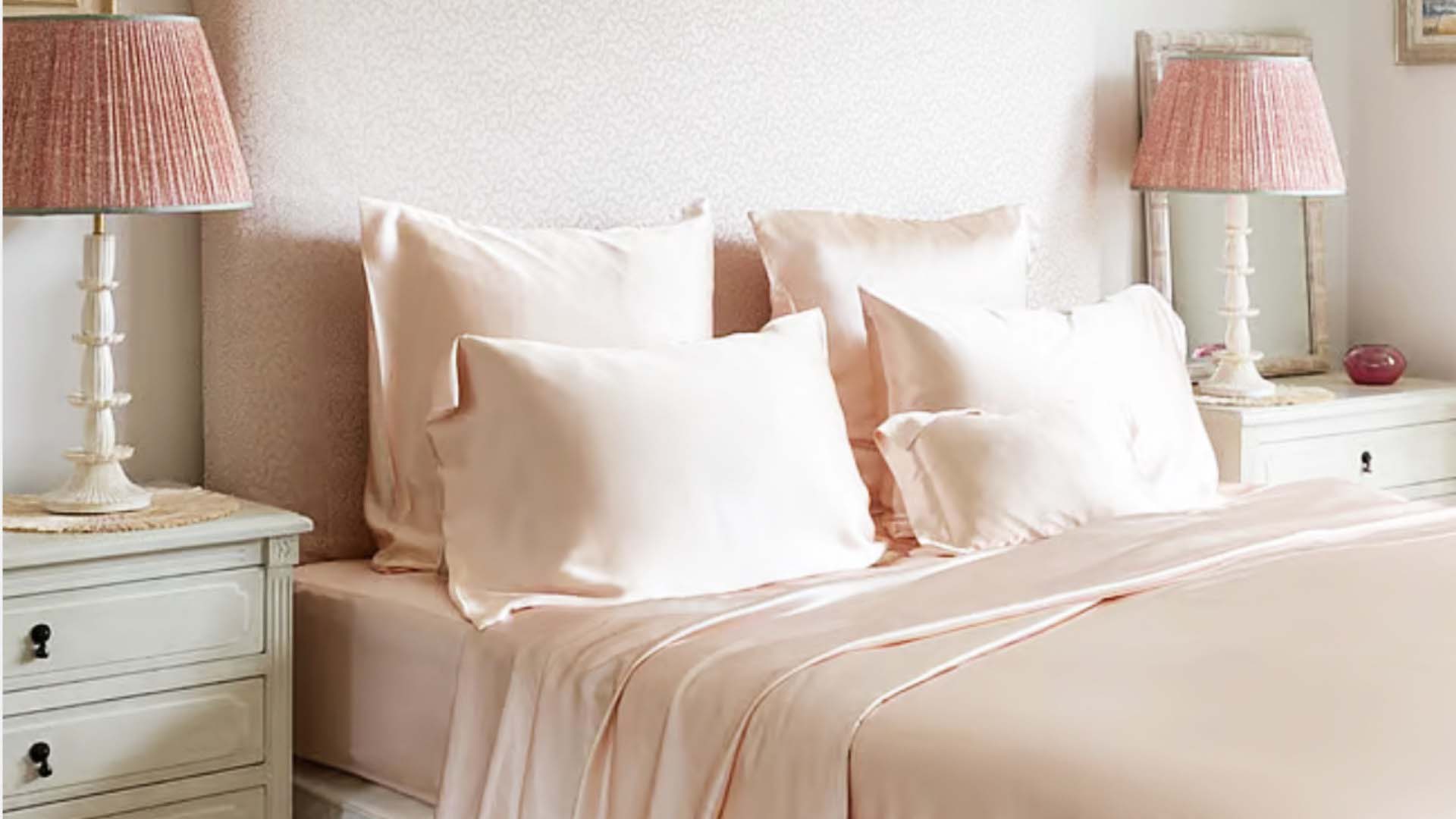 pink satin sheets on a bed with bedside tables and lamps