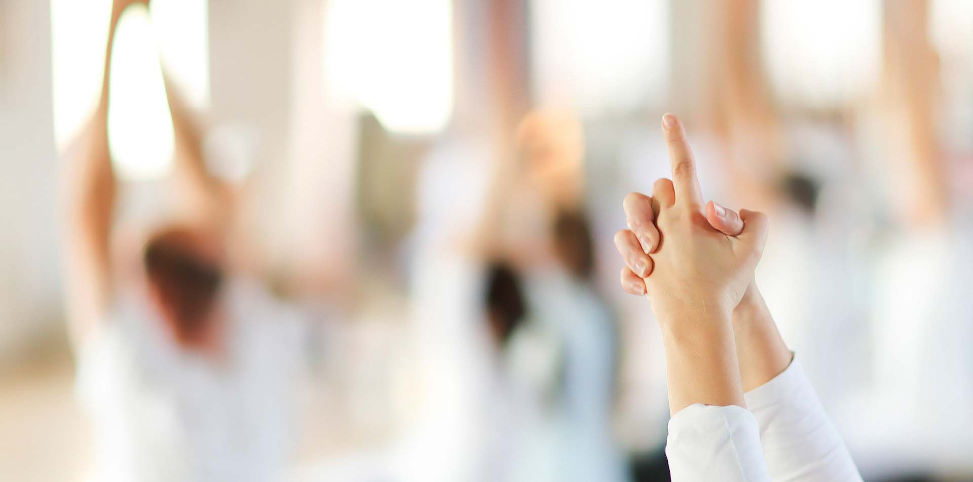 Close-up of a person's arms above their head with palms pressed together and index finger pointed upwards while practicing yoga.