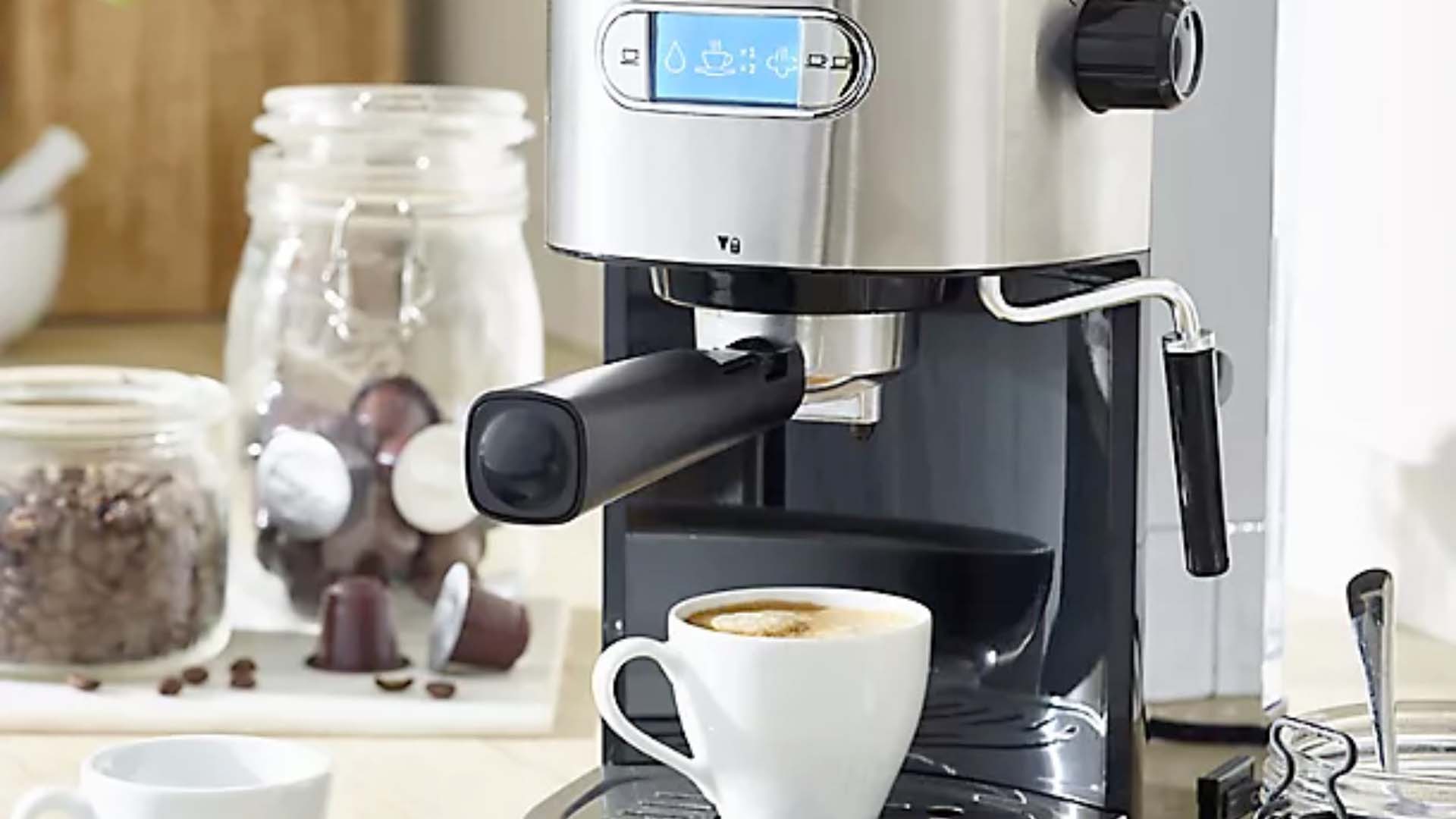 A coffee machine with a mug of espresso and jars of coffee beans in the background.