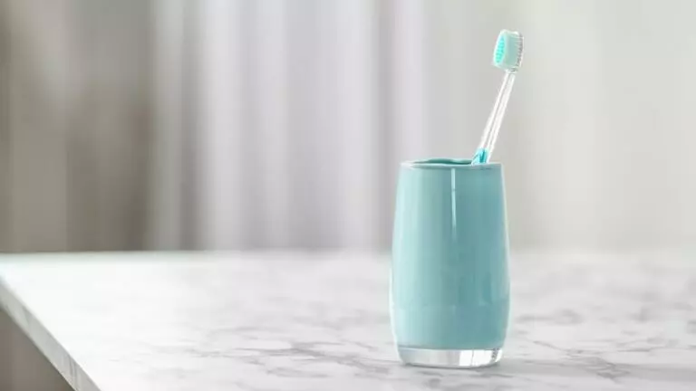 Manual toothbrush sat in a cup in a bathroom
