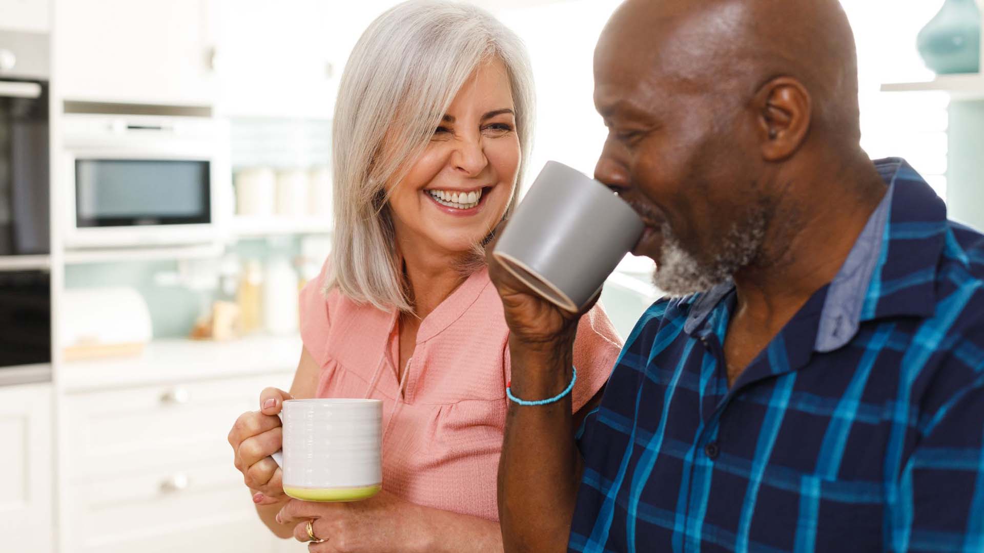 A mature interracial couple drinking from coffee mugs in a kitchen setting