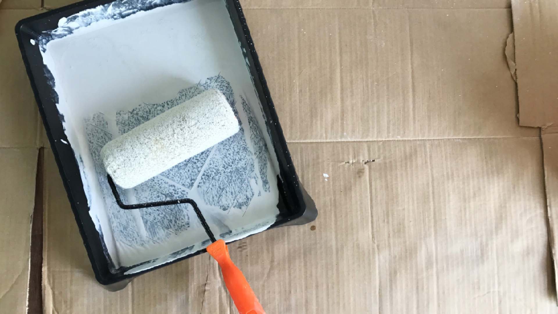 A paint tray filled with white paint and a paint roller