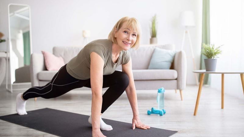 A woman performing a runner's lunge on a yoga mat indoors