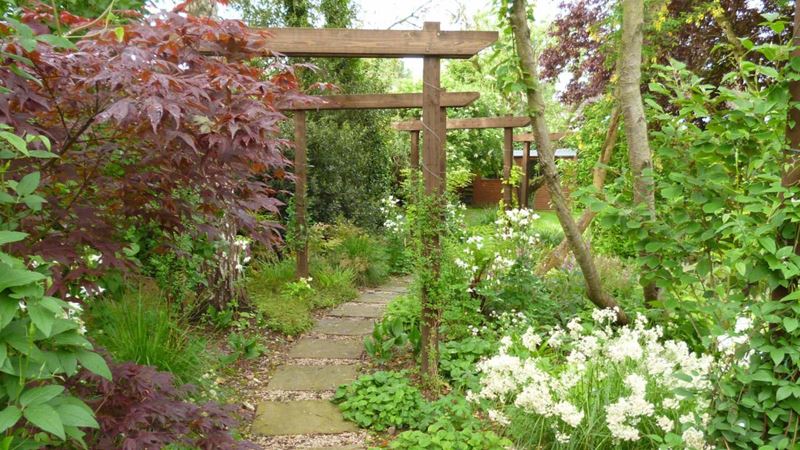 Pretty curved garden path flanked by bushes, trees and flowers