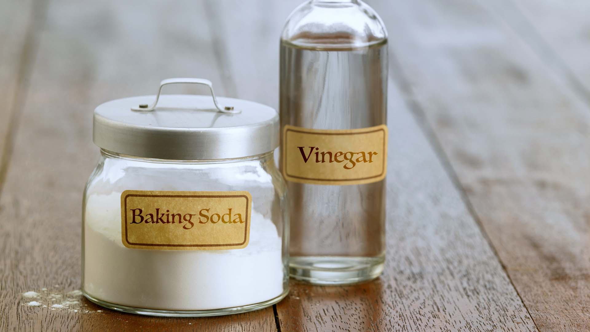 A pot of baking soda and bottle of vinegar on a wooden counter, both with vintage labels