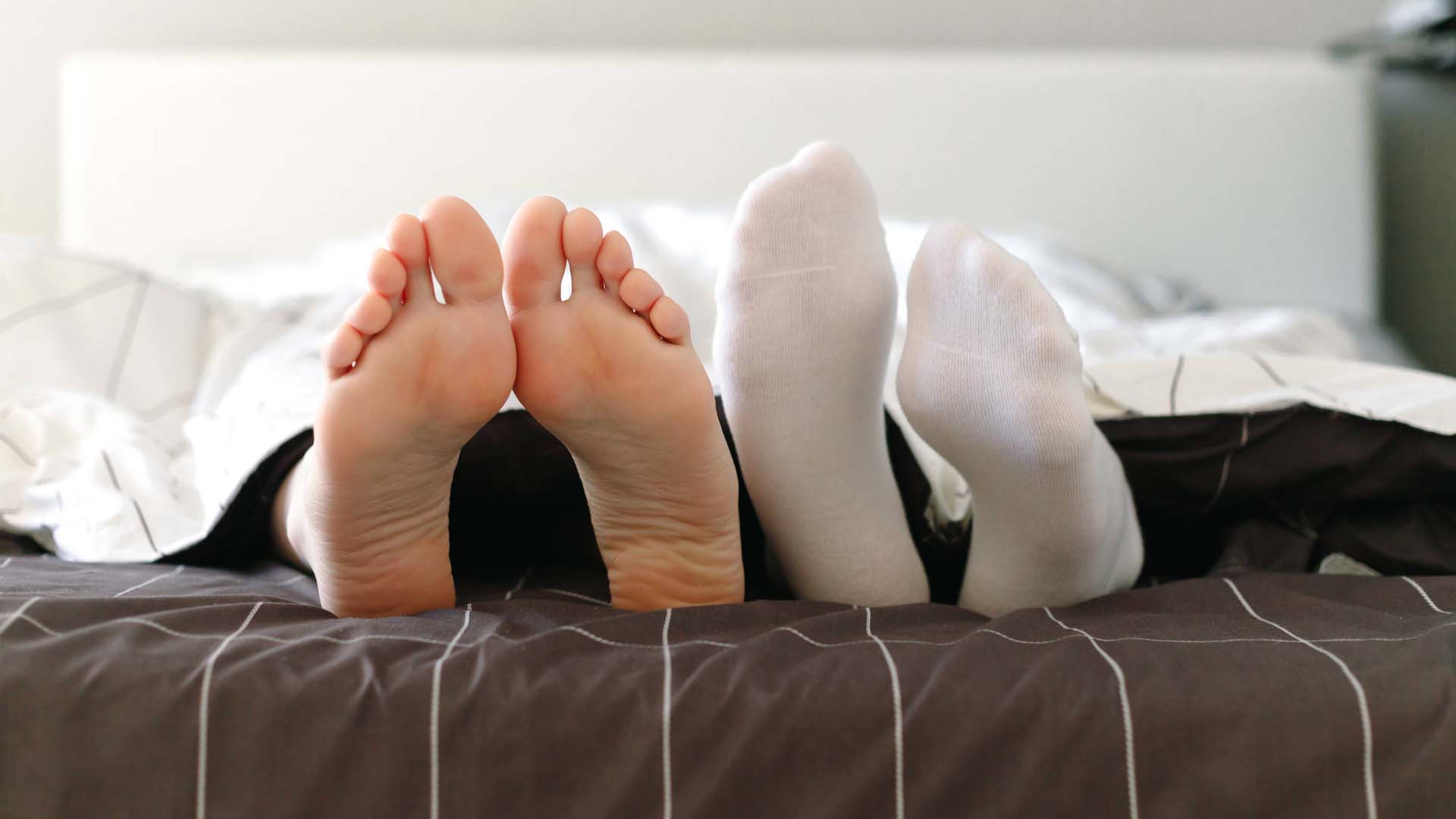Two people in bed, one sleeping with socks on, the other in bare feet