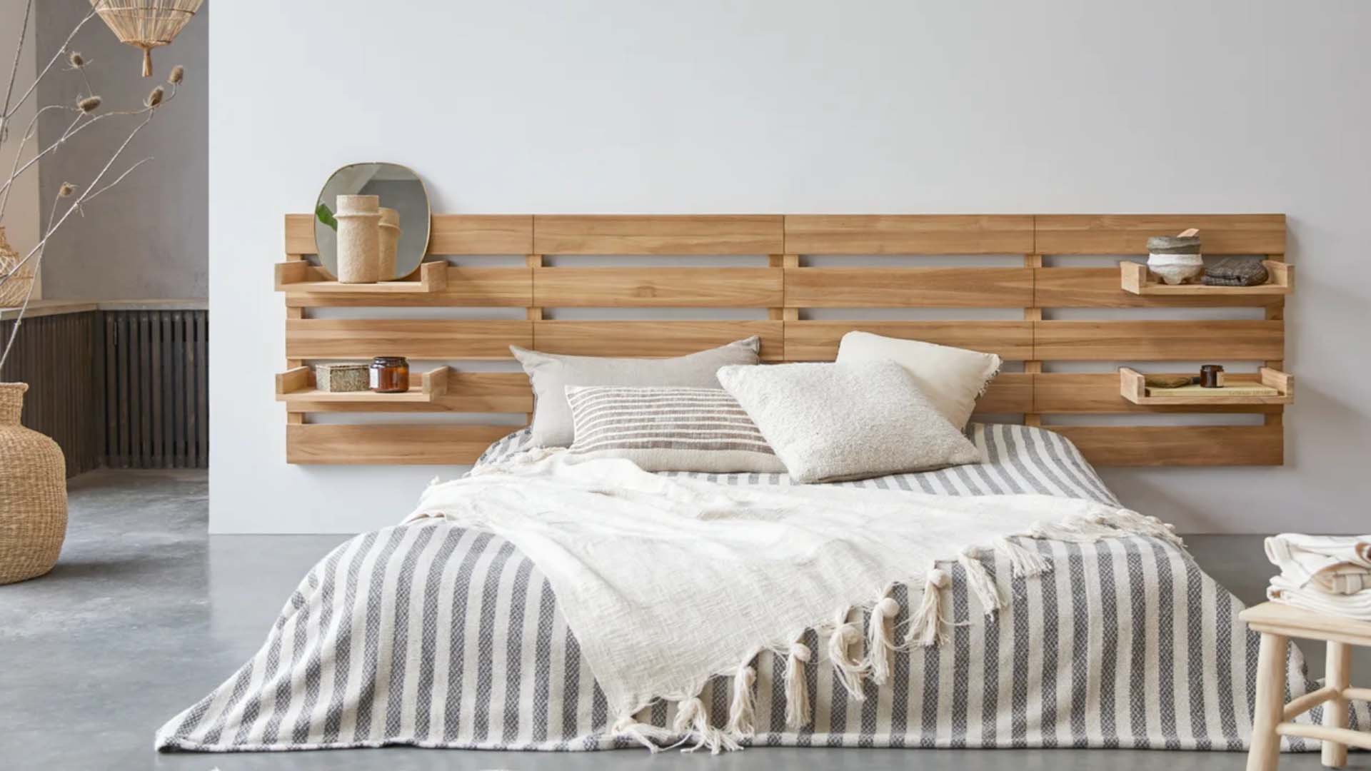 A slatted wooden headboard with built-in shelves and a large bed dressed with soft furnishings