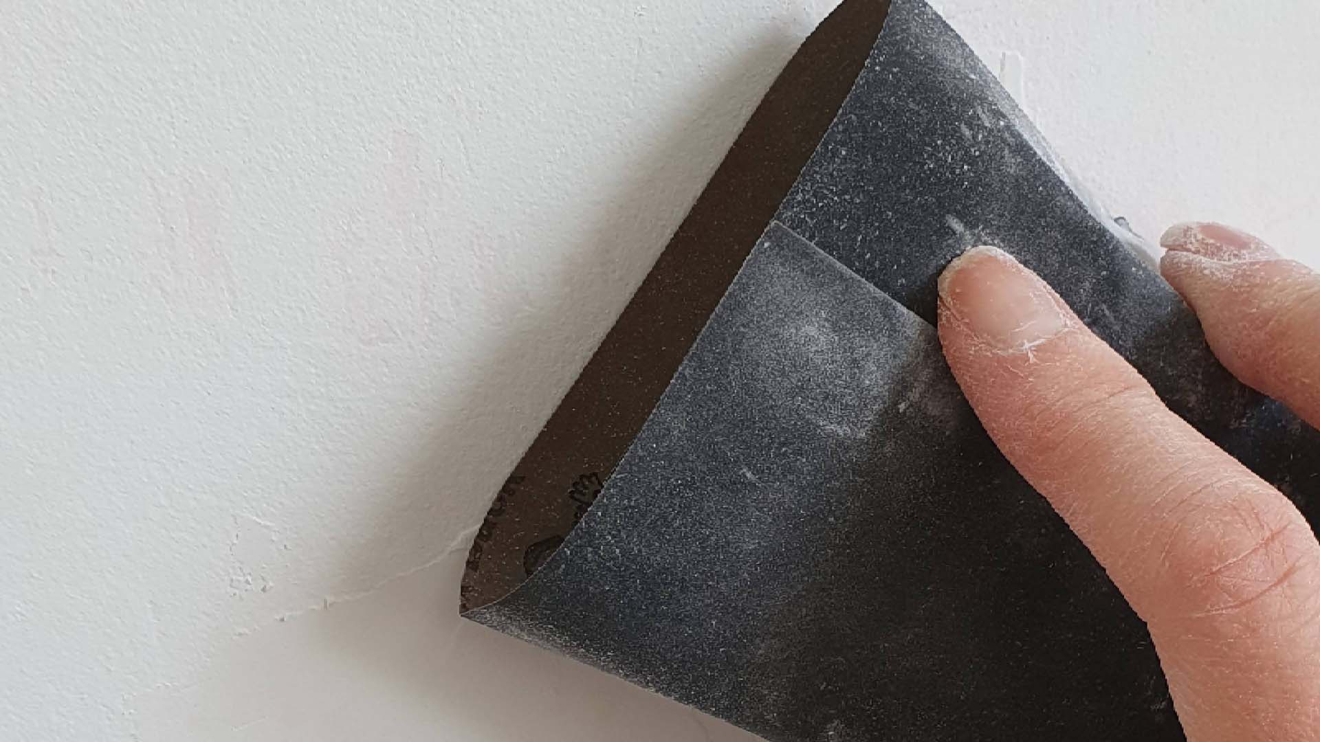Close-up of someone sanding a wall with a block covered wrapped in course sandpaper