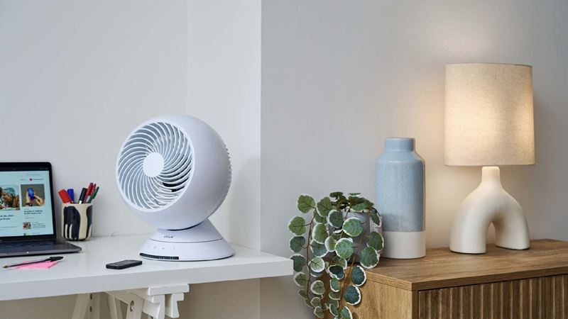 A Duux globe fan on a counter with a lamp and a plant