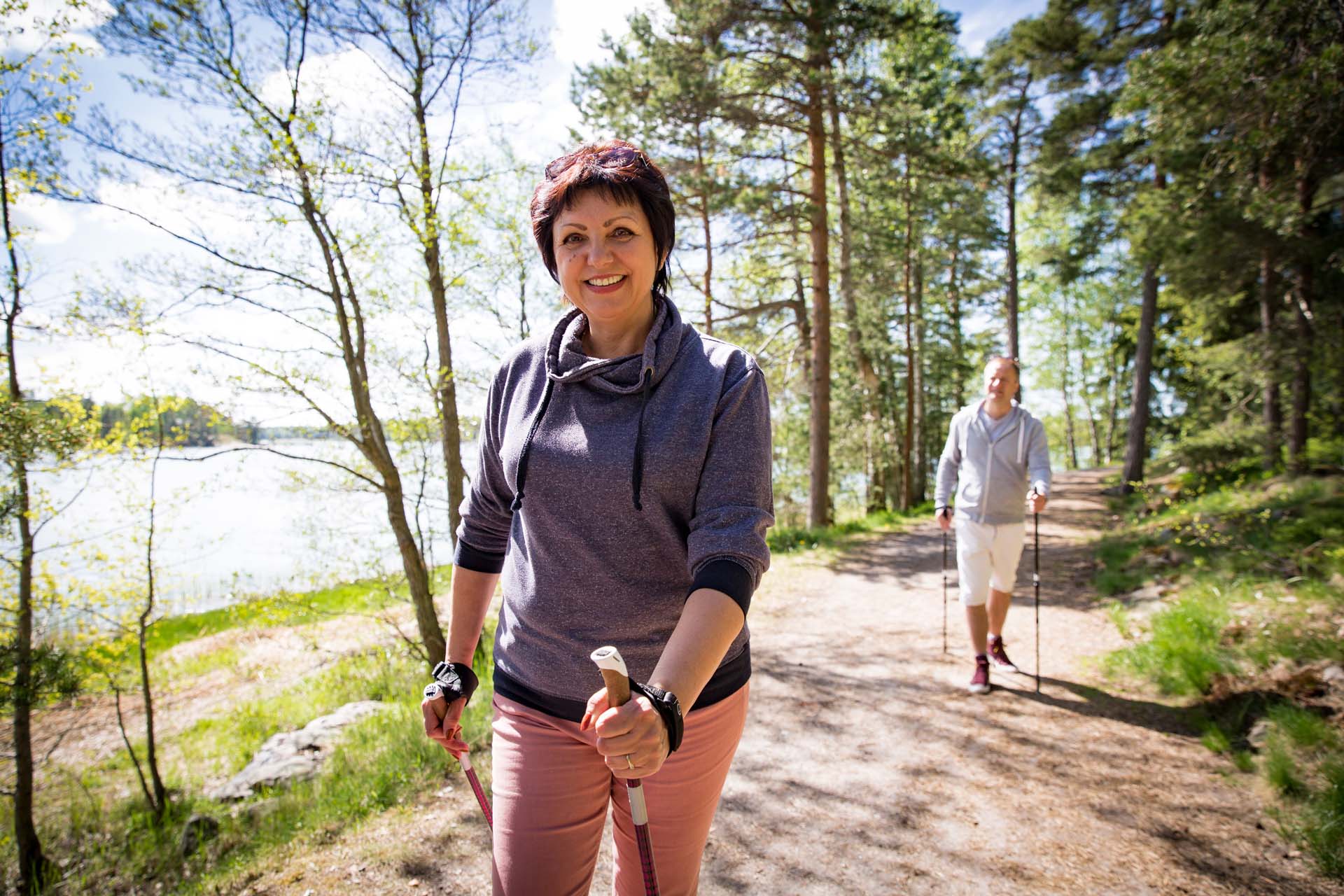 A woman and a man walking next to water through woods