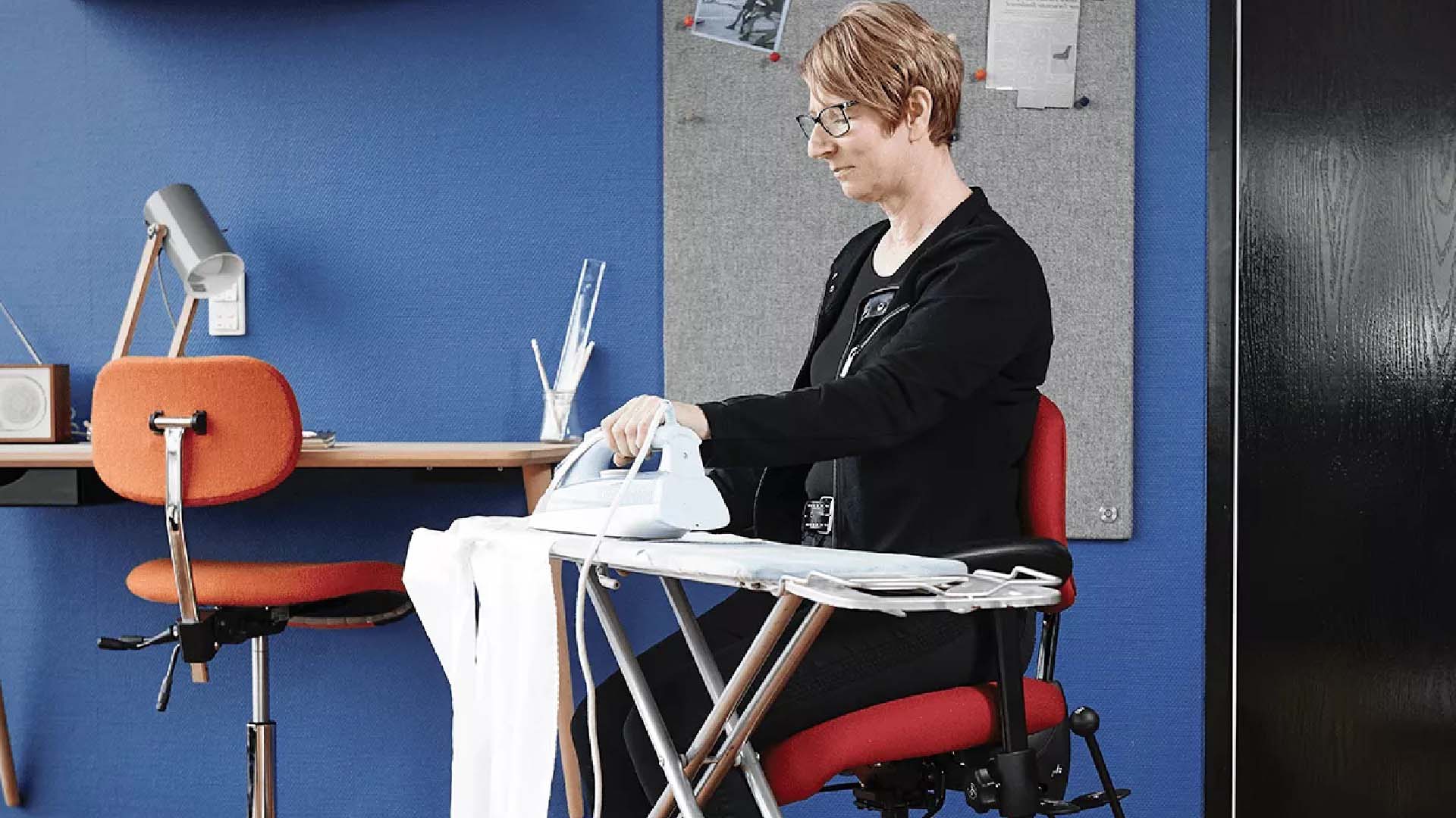 Woman sitting at an ironing board on a desk chair