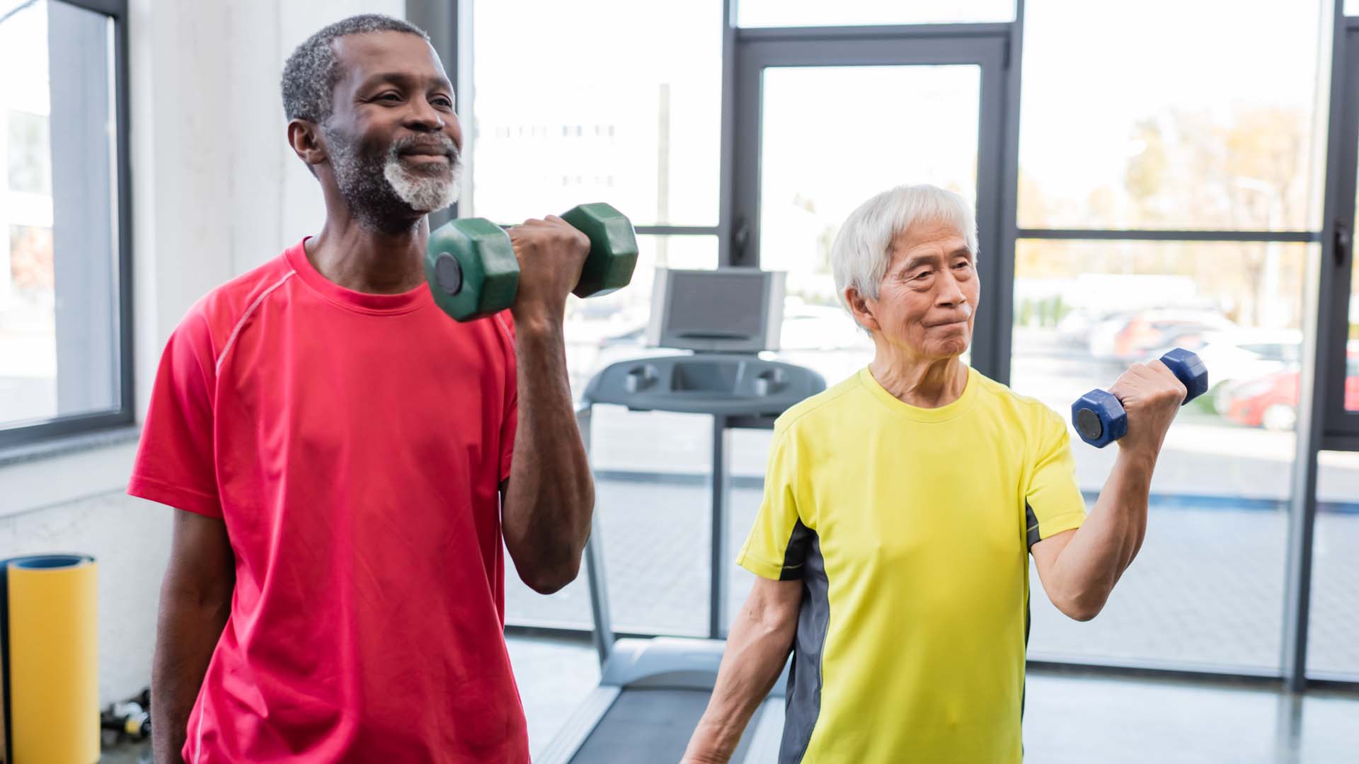 Two older men lifting hand weights in a gym setting
