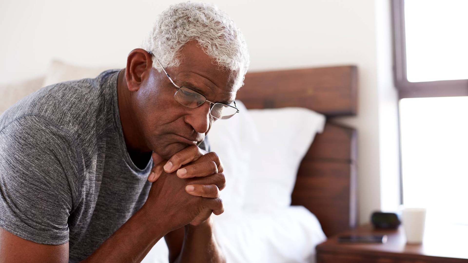man sat on the edge of his bed with his hands clasped