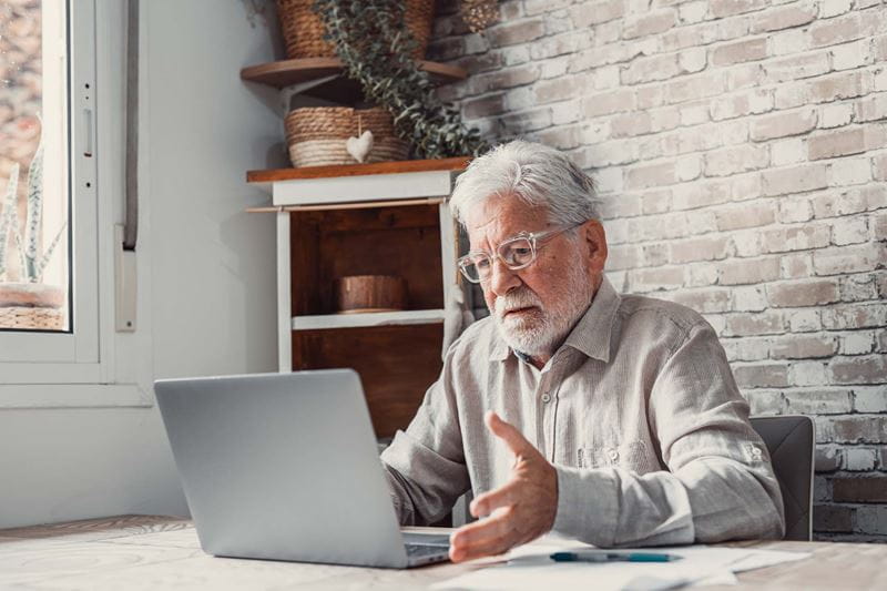 A mature man sitting in front of the laptop looking confused
