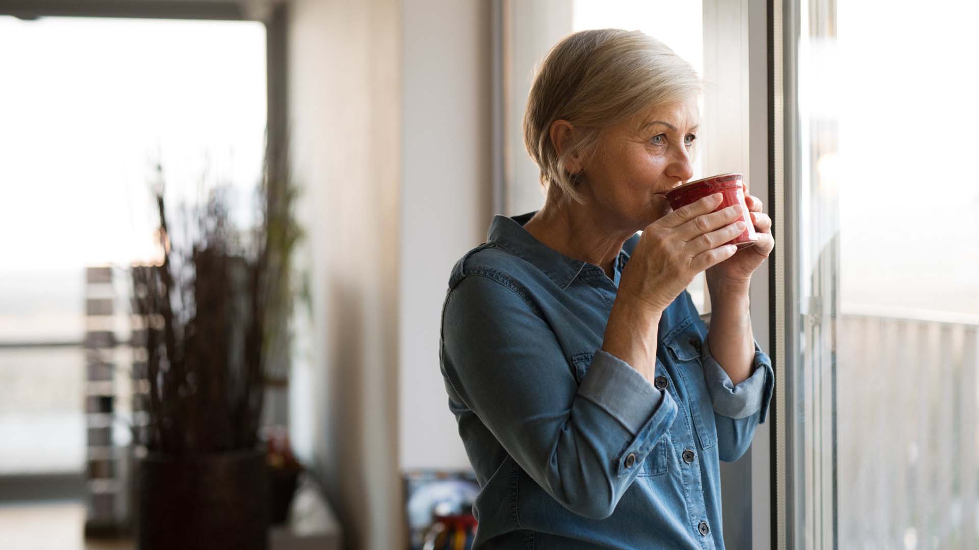 Senior woman at the window holding a cup of coffee