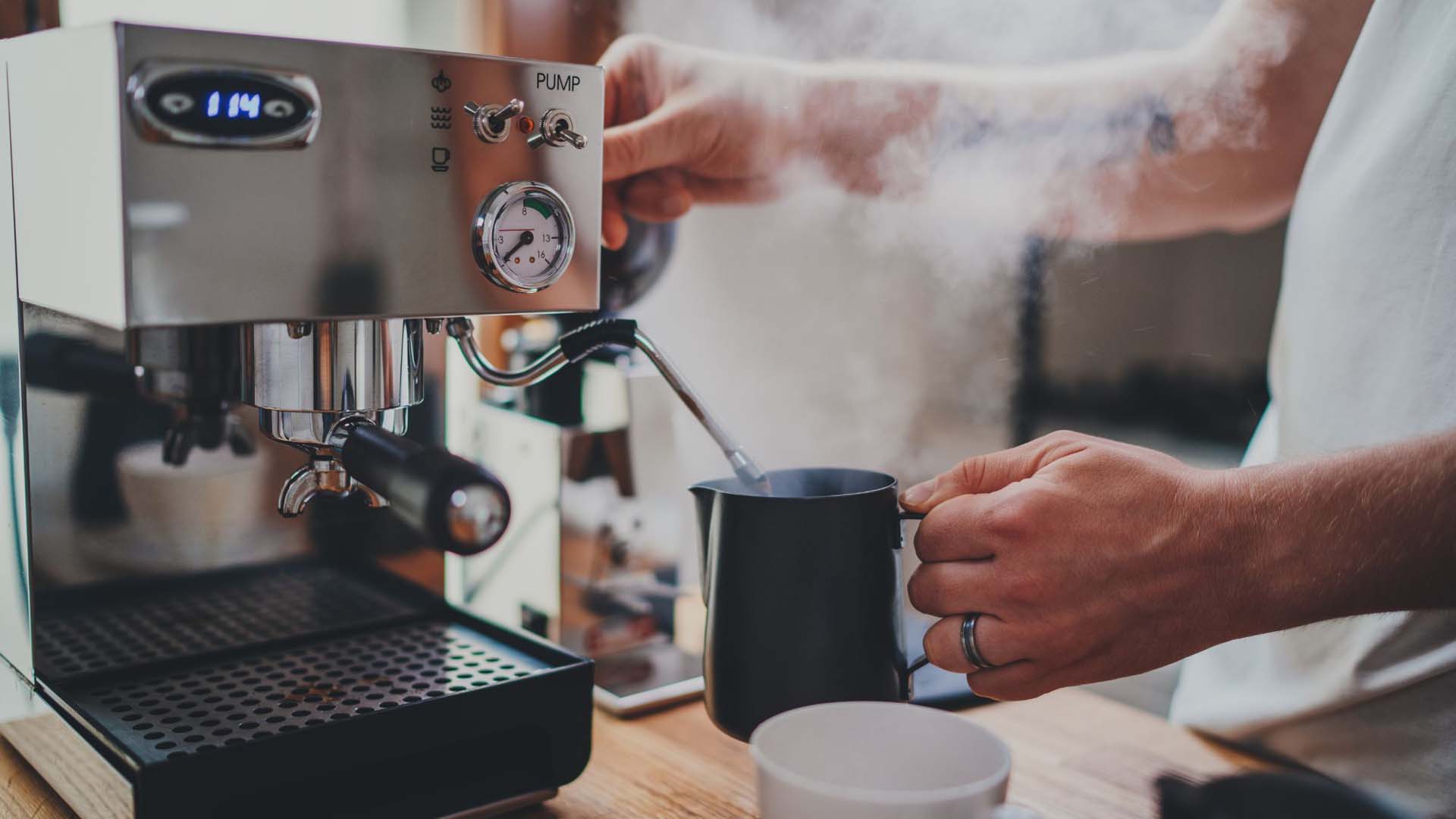 Close-up of a barista frothing milk in a silver jug at a professional coffee machine
