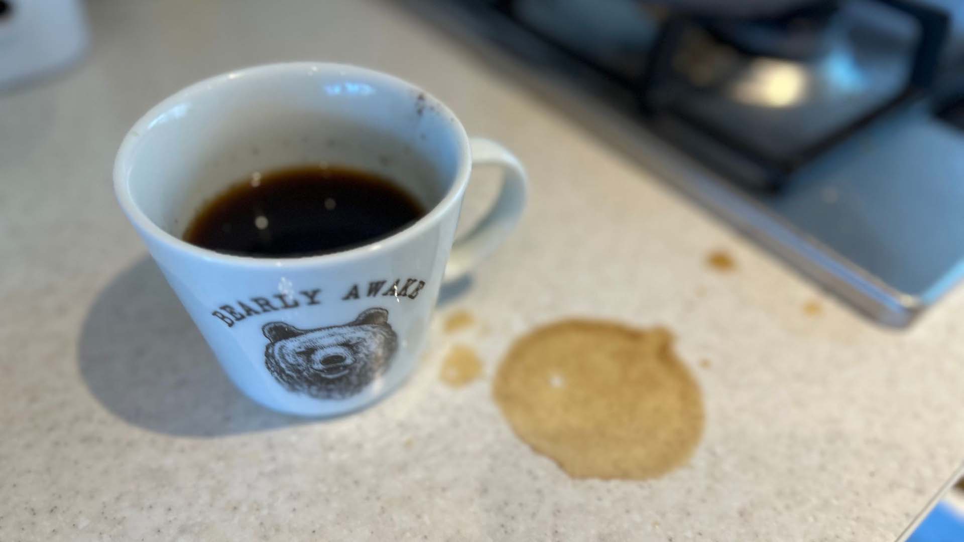 A coffee cup with spilled coffee next to it on the counter