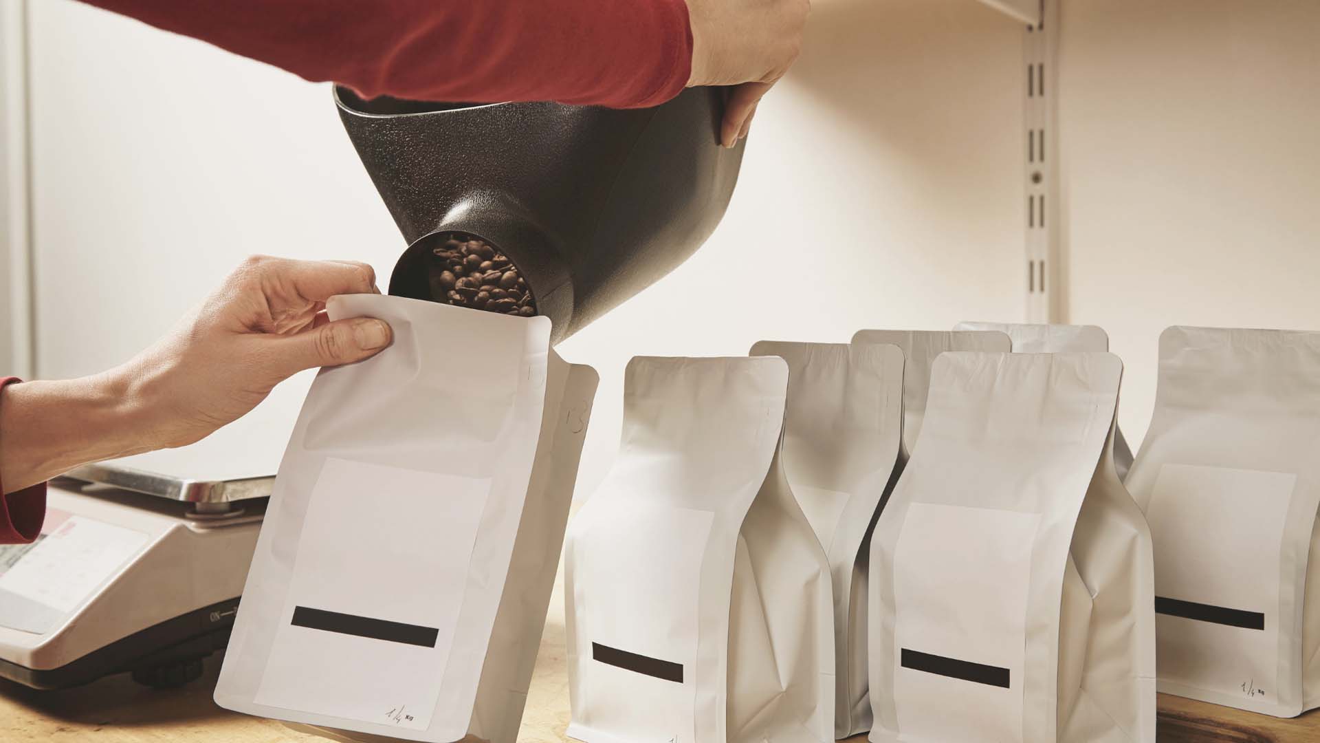 Close-up of someone hand-filling white bags with coffee beans