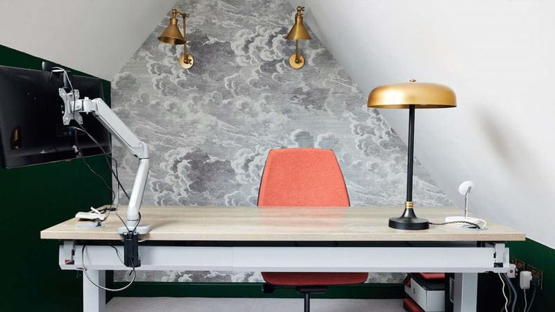 A small attic room converted to a study with a desk, lamps and stylish wallpaper
