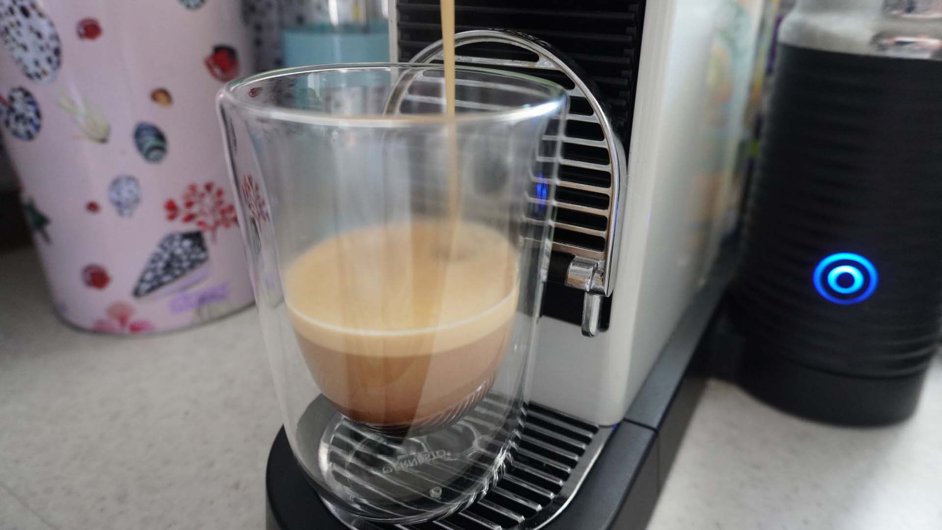 Close-up of coffee pouring out of a coffee pod machine into a clear espresso mug
