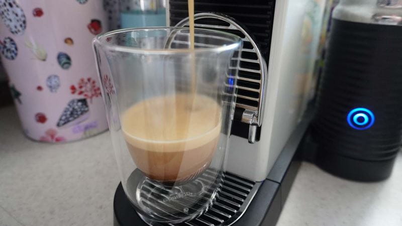 Close-up of coffee pouring out of a coffee pod machine into a clear espresso mug