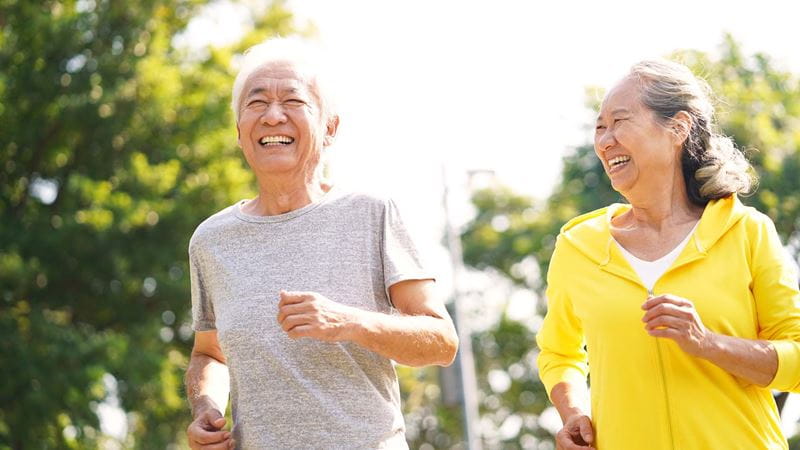 an older man and woman jogging together outdoors in the sunshine smiling