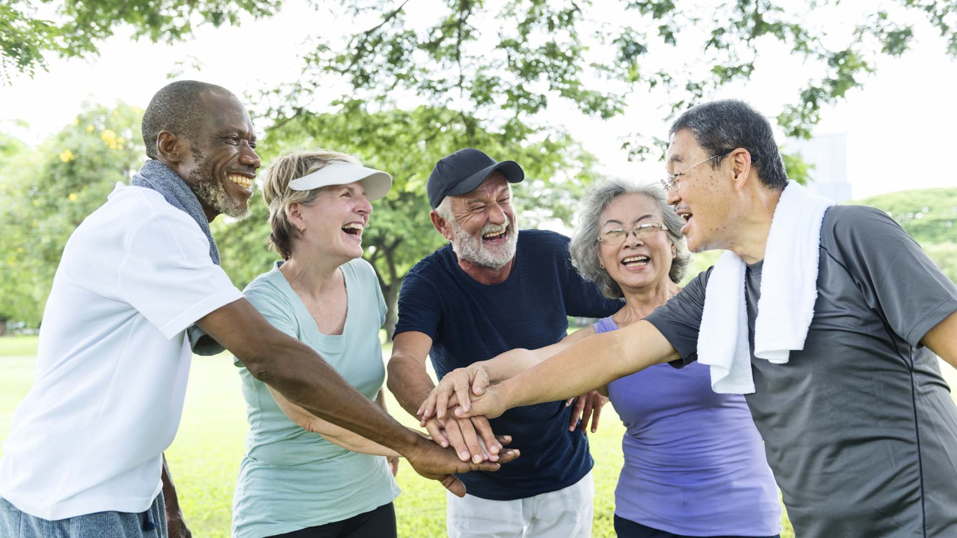 Five adults wearing athleisure smiling and coming together after exercise 