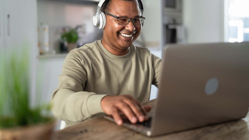 A man on a laptop smiling with headphones on