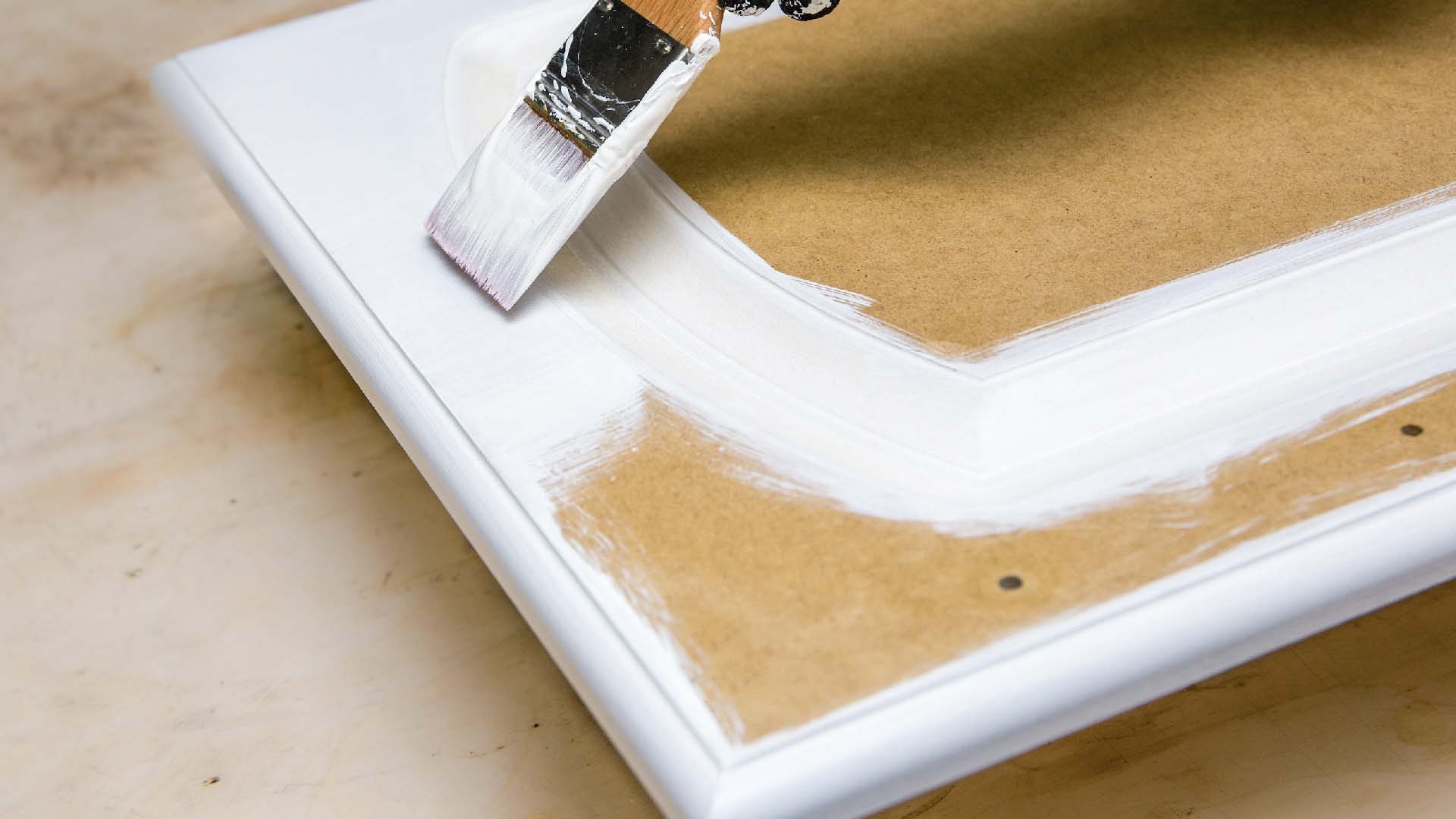 Close-up of painting a piece of MDF wood with white paint.
