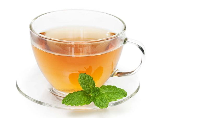 a glass teacup and saucer with peppermint tea and a peppermint leaf on the side