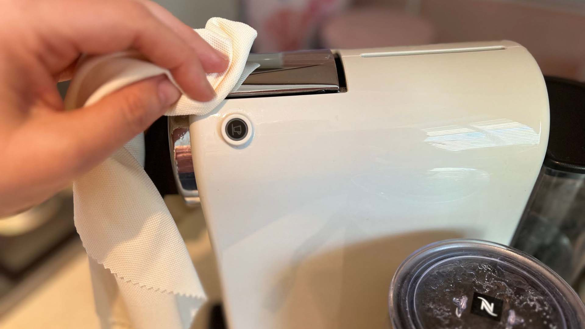 Close-up of someone using a soft cloth to wipe the surface of a coffee pod machine