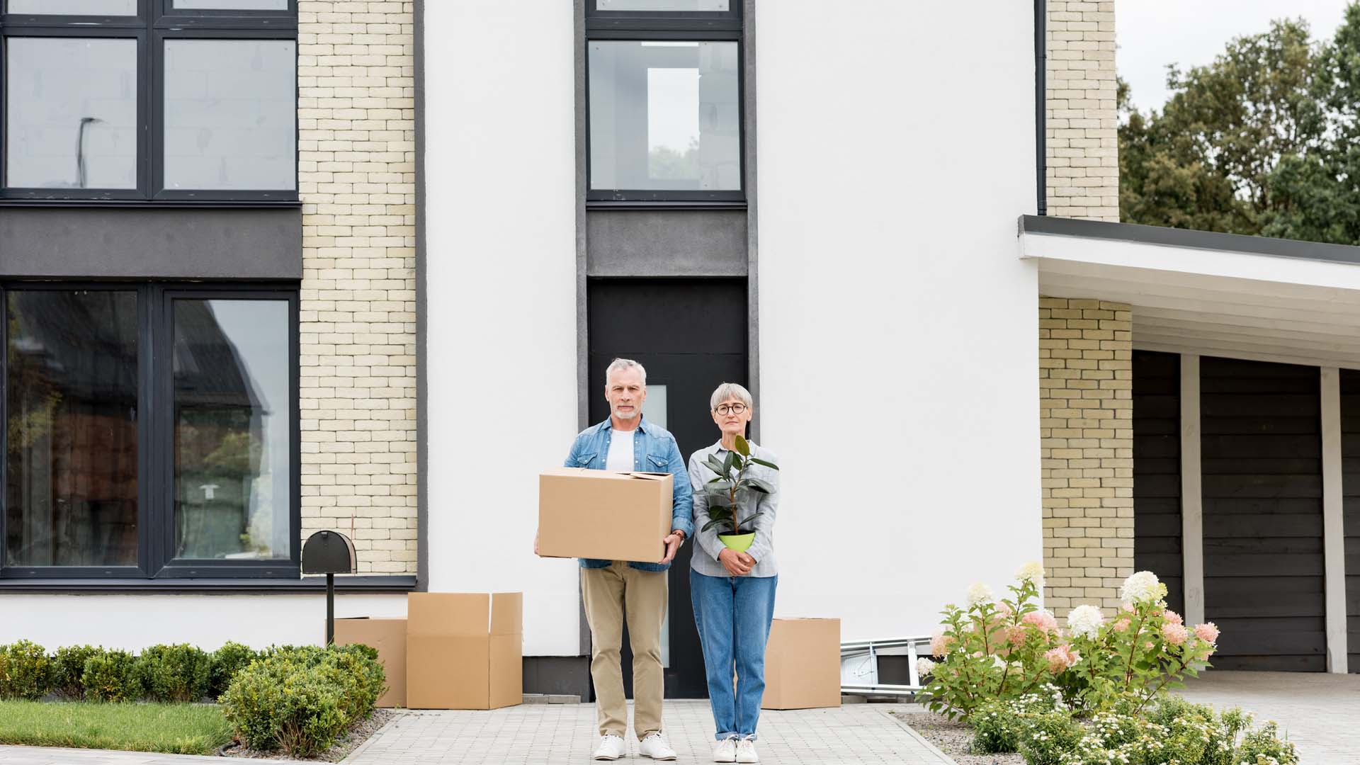 A couple stand outside a house with moving boxes