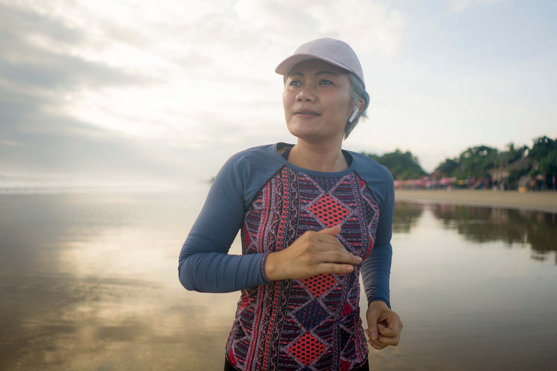 A woman wearing a cap and sports attire running past a body of water on a sunny day