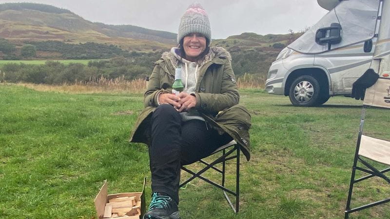 Siobhan Daniels on a camping chair in a field with her motorhome in the backgrou