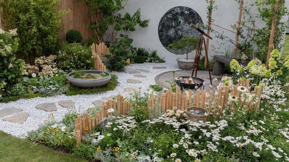 A winding gravel path, circle paving with planted beds in both sides. The pathway features grey, paddlestone stepping stones surrounded by meadowgrass marble aggregate