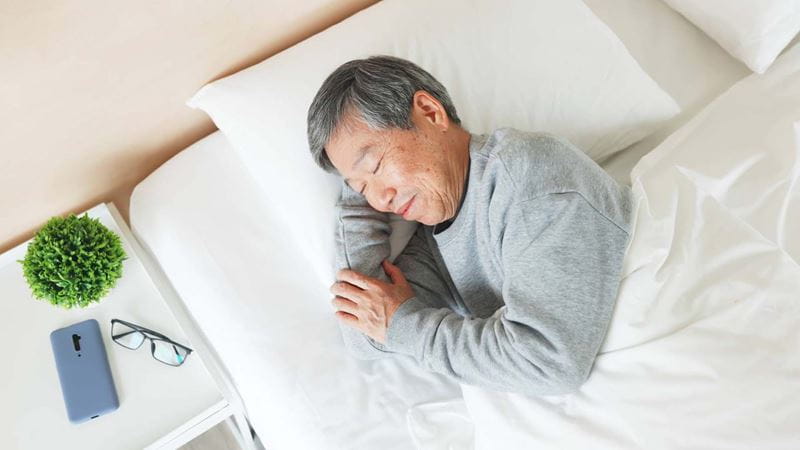 top view of asian senior man lying on bed sleep well with smile in bedroom at home