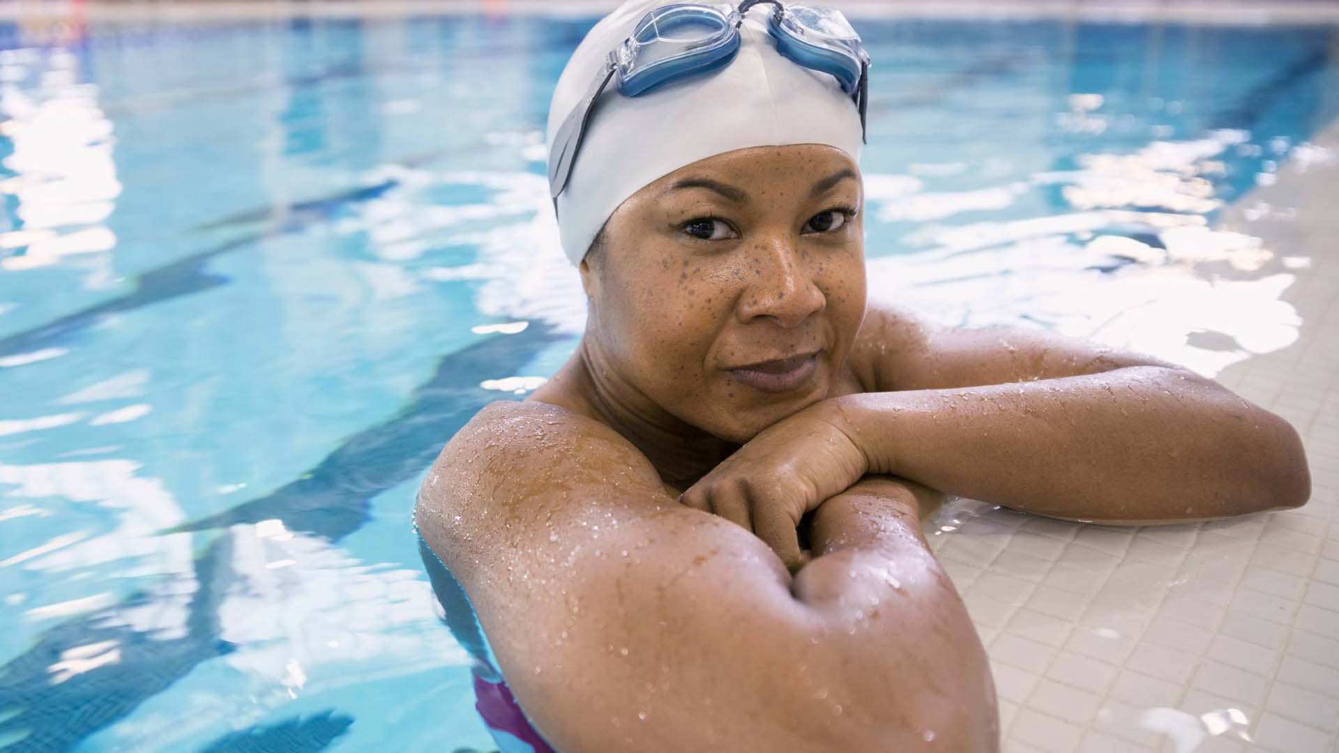 woman in a pool on the edge with goggles and a cap