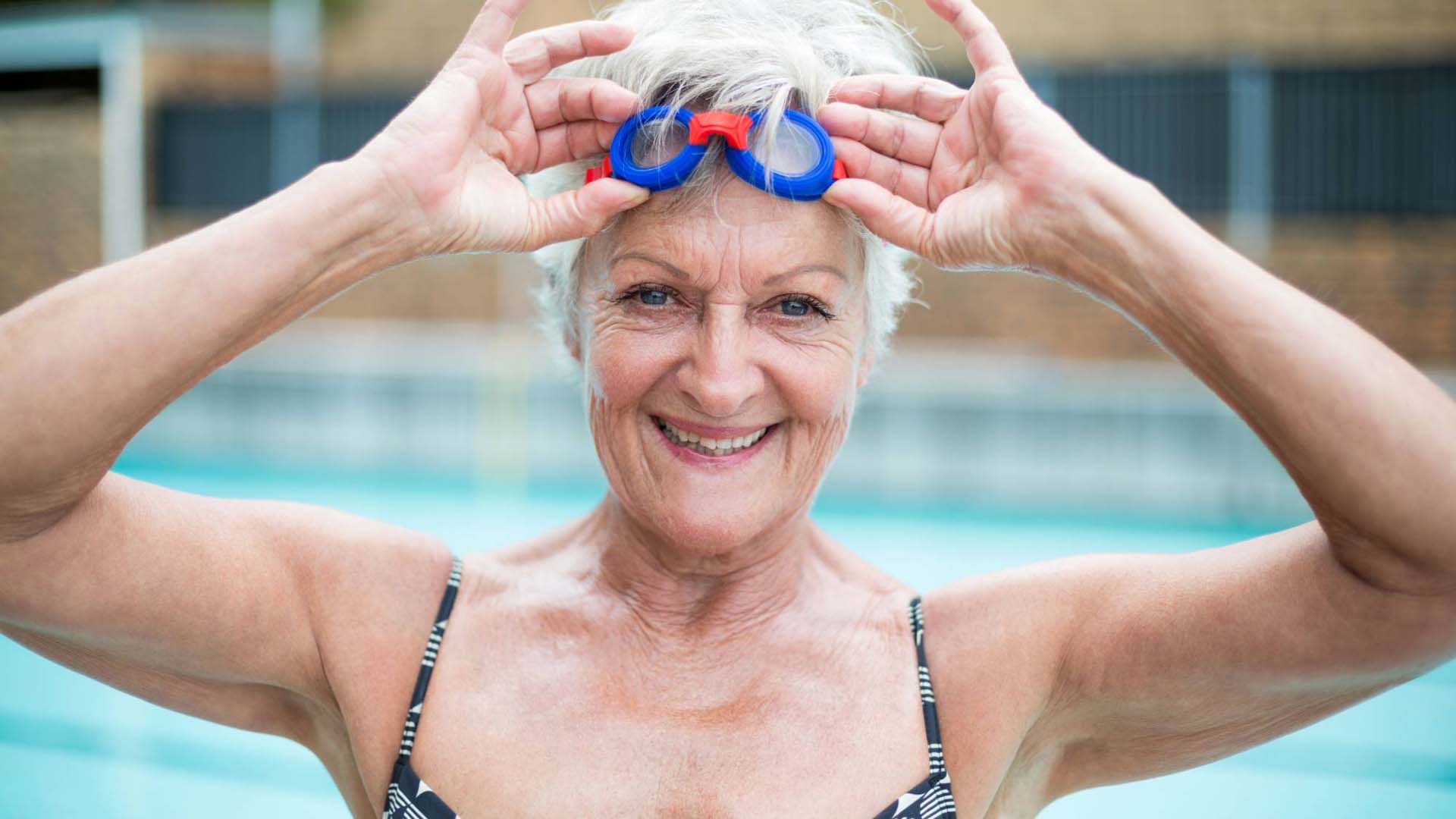 woman by the swimming pool holding onto her goggles