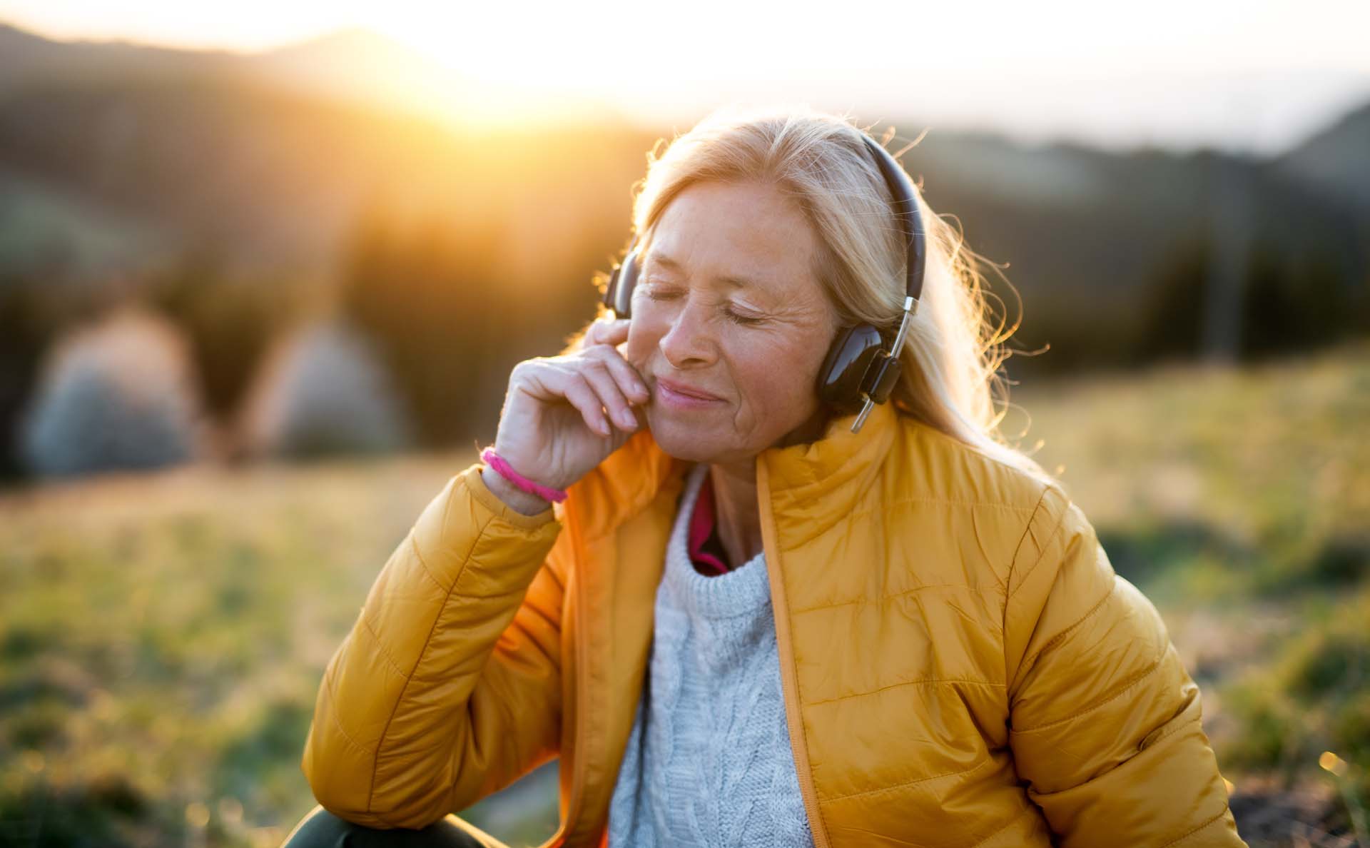 A woman outside smiling and listening to something on her headphones
