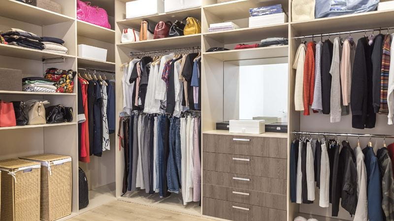 A walk-in wardrobe with fitted cupboards, drawers and shelves, which are filled with clothes.