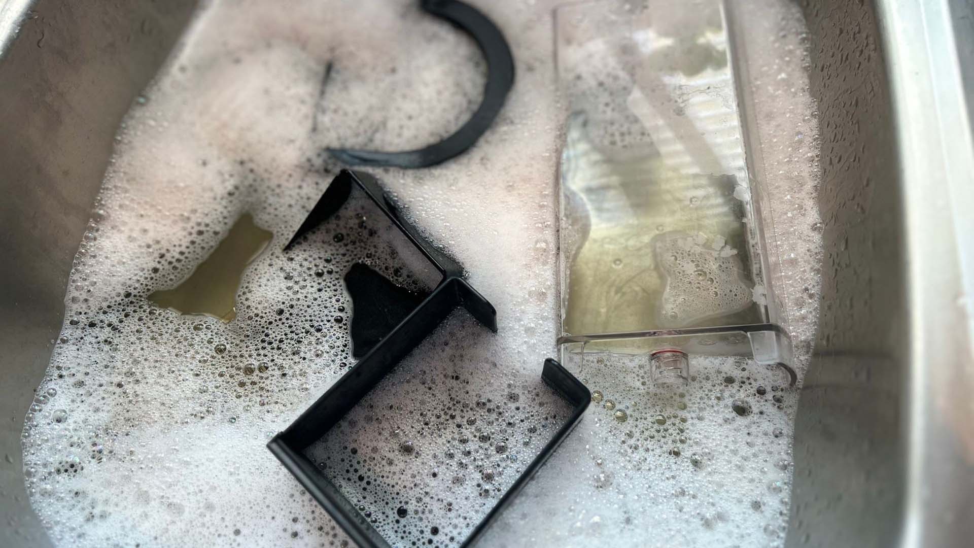 Close-up of coffee pod machine pieces soaking in soapy water in a sink