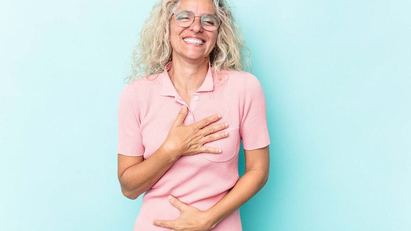 A smiling woman in a pink top holding her stomach